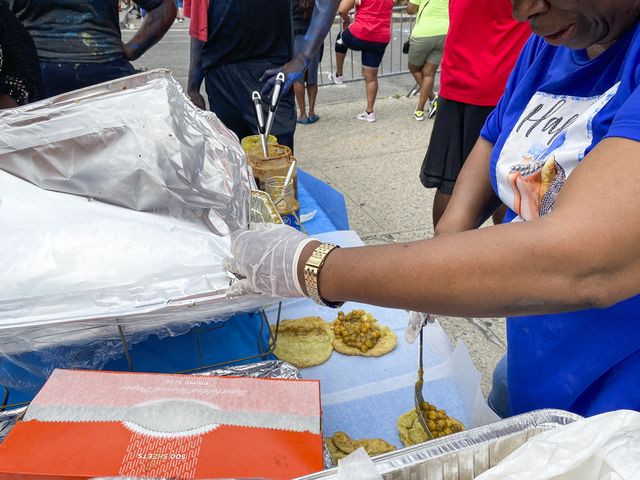 A woman prepares doubles by putting spiced chickpeas on small pieces of fried dough. The Trinidadian snack is being served during the J'Ouvert festival in Brooklyn on Monday, September 5, 2022.